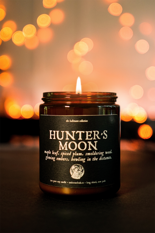 an amber jar candle sits in front of glowing orange lights with a textured black paper label that reads "hunter's moon"