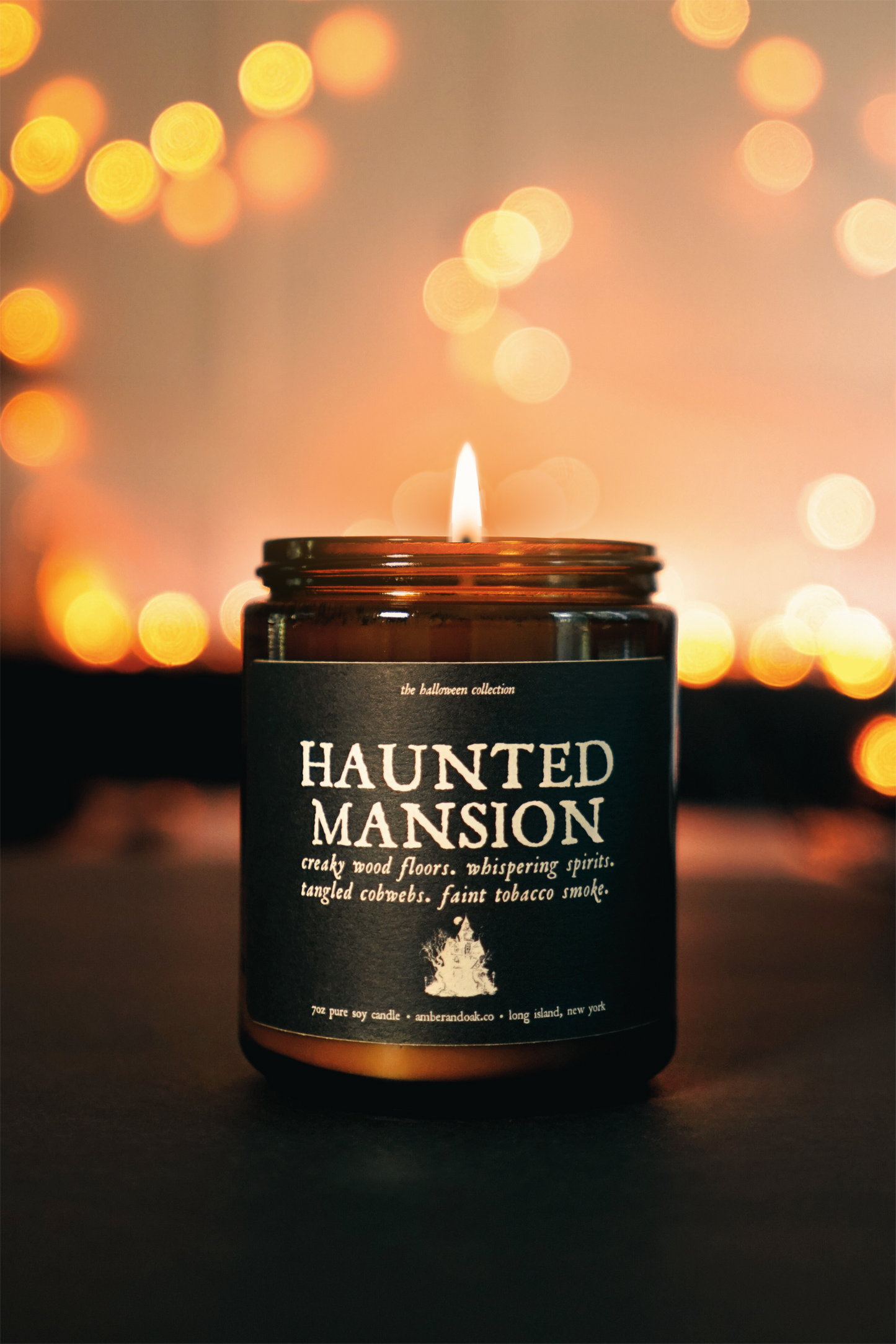 an amber jar candle is lit, sitting in front of glowing orange lights. the textured black label reads "haunted mansion".