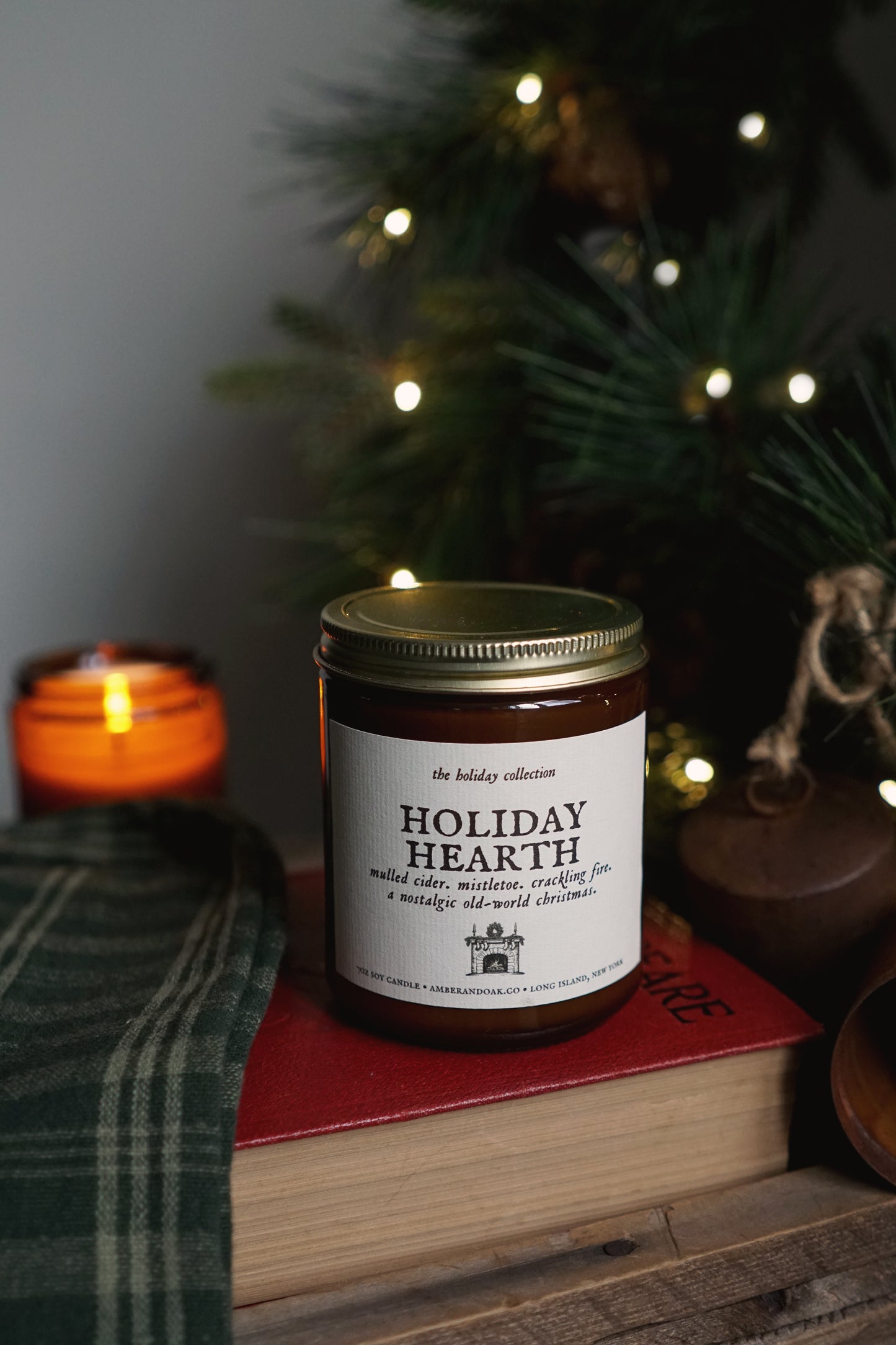 holiday hearth candle sitting on top of a book with a lit evergreen in the back