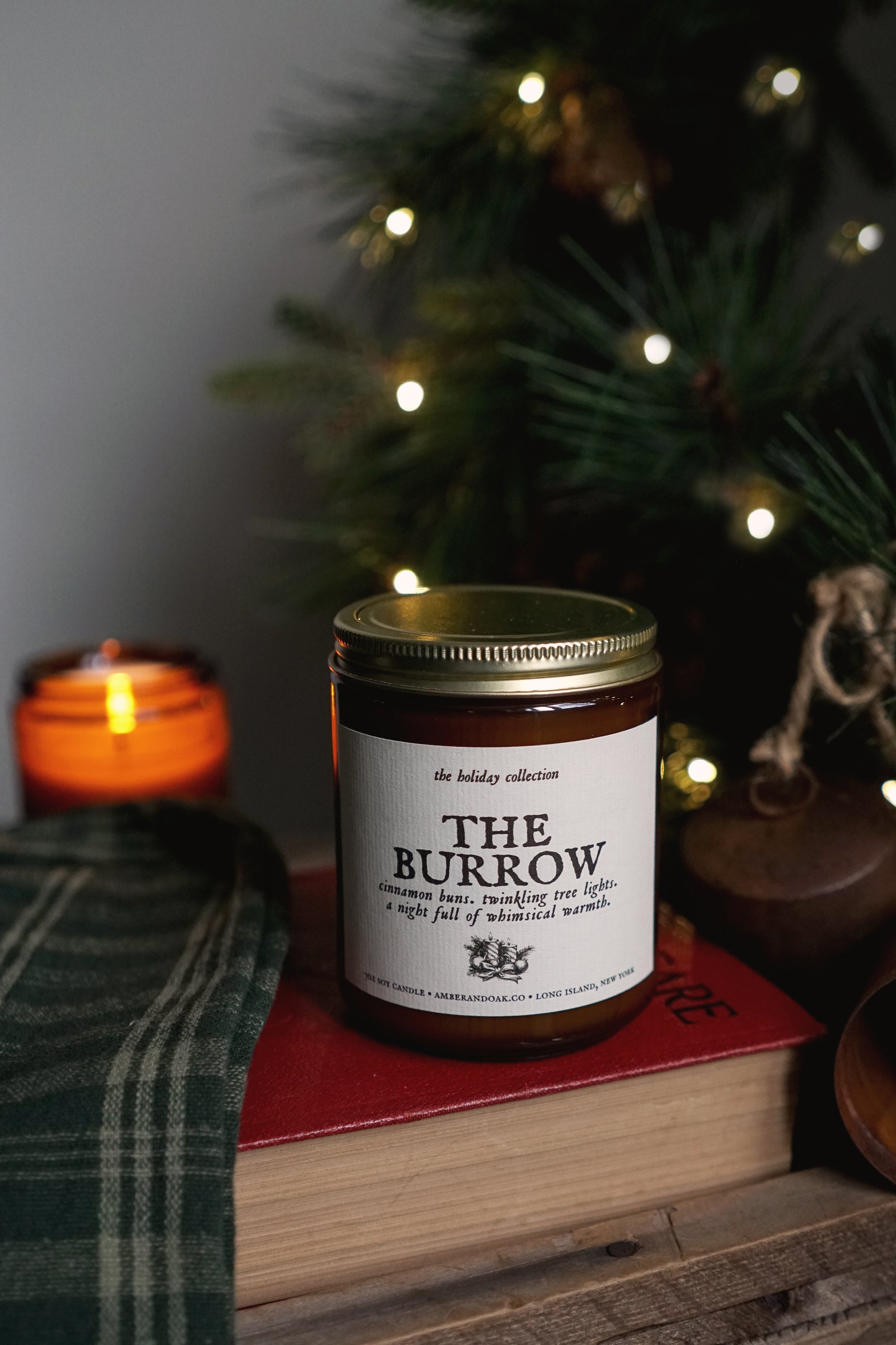 the burrow candle sitting on top of a book with a lit evergreen in the back